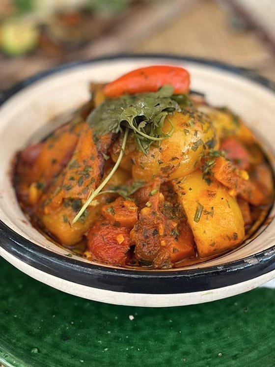 A Moroccan tagine of vegetables and herbs served on a green ceramic plate.