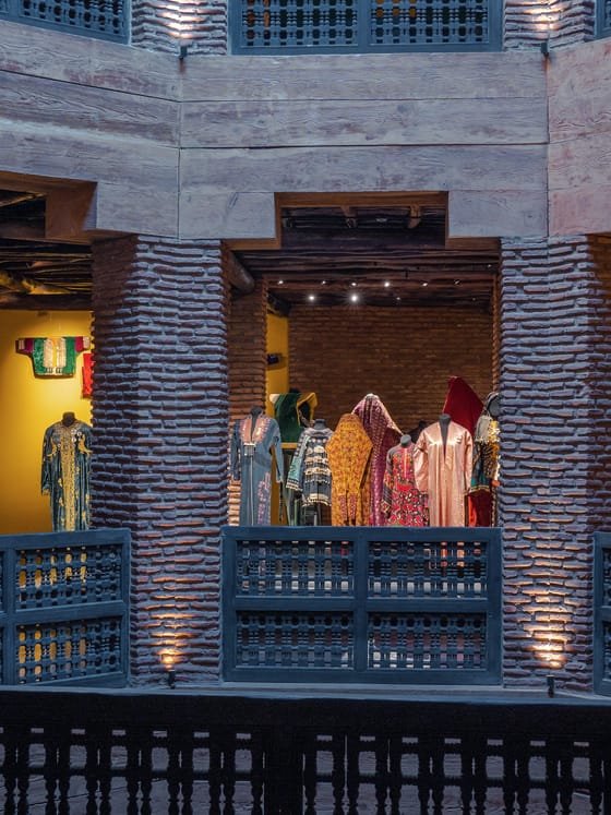 Historic Moroccan caftans displayed in a museum's brick-columned galleries.